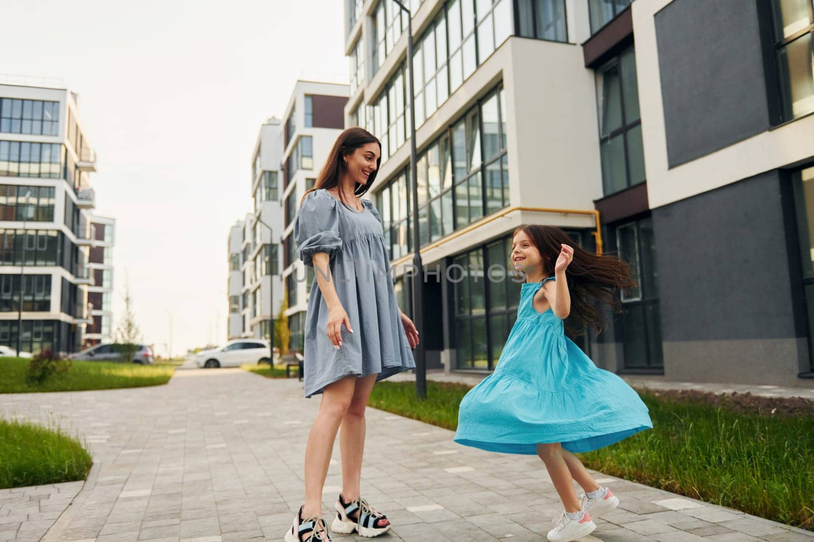 Young mother with her little daughter walking near the buildings.