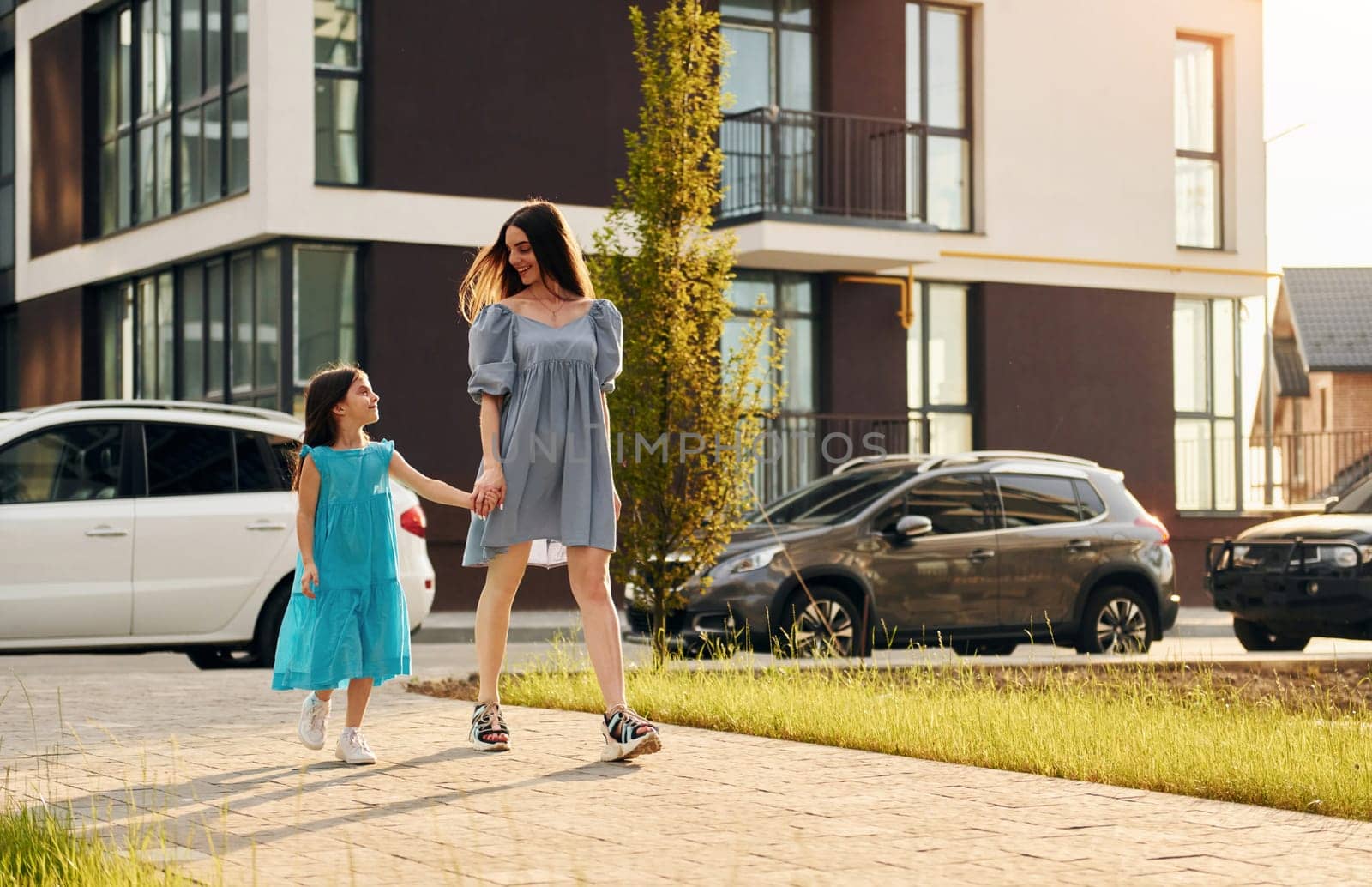 Young mother with her little daughter walking near the buildings.