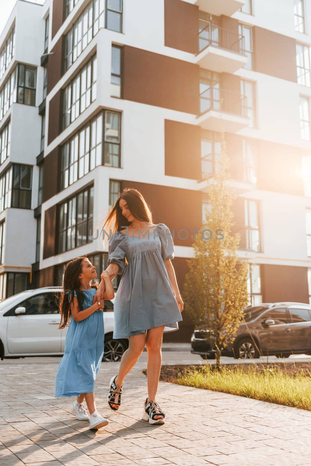 Illuminated by sunlight. Young mother with her little daughter walking near the buildings.