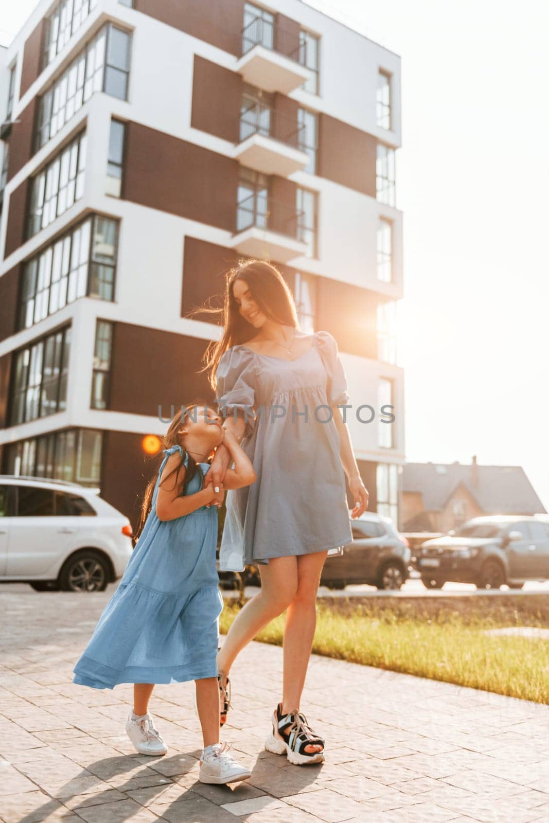 Illuminated by sunlight. Young mother with her little daughter walking near the buildings.