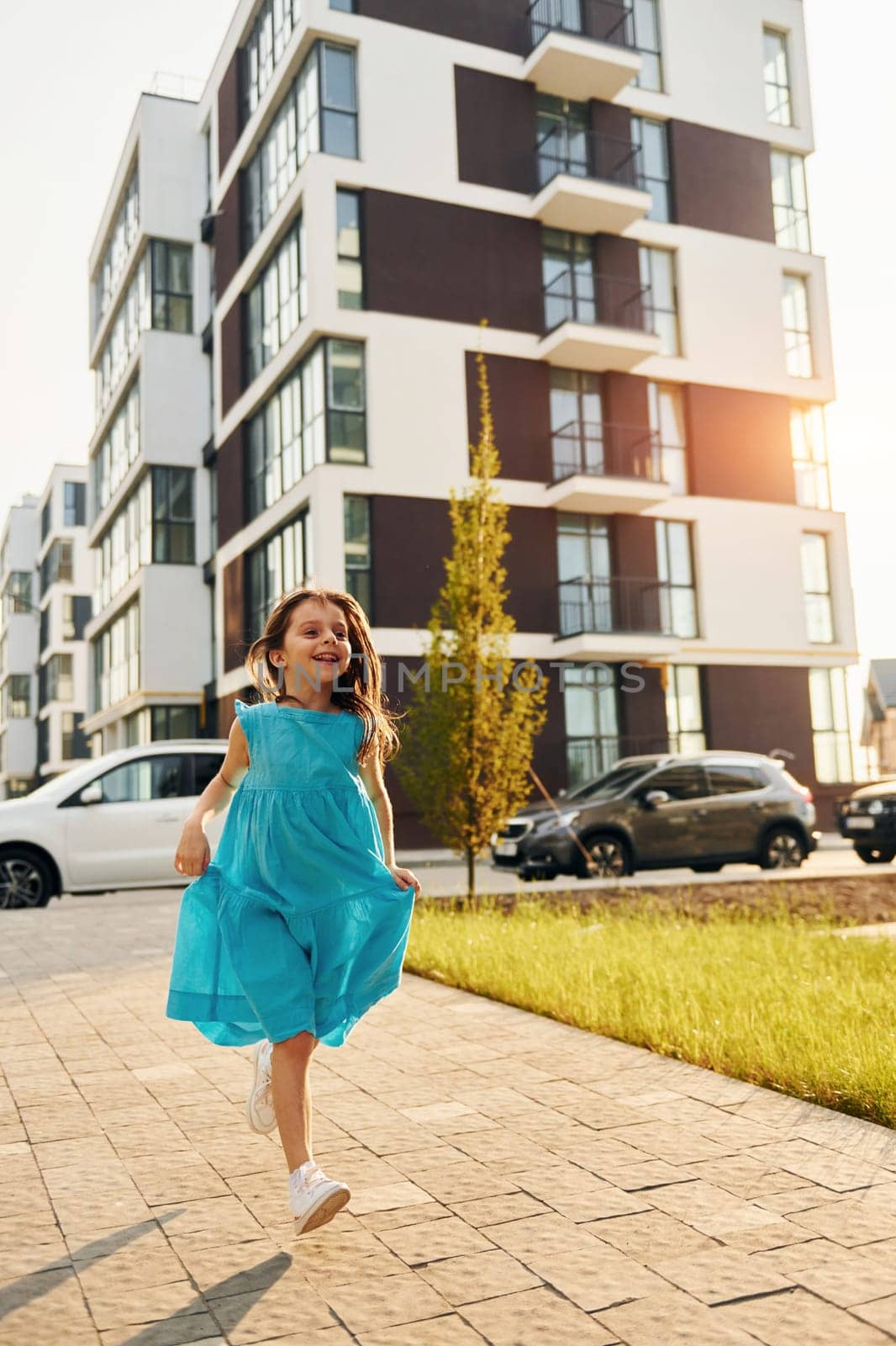 Cheerful little girl walking outdoors in the city in dress.