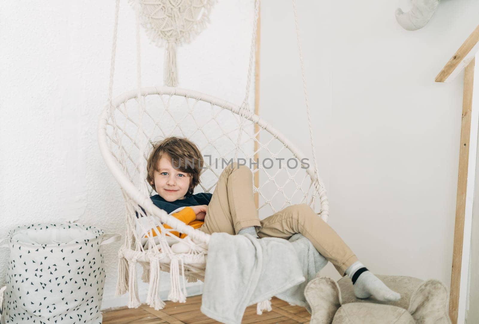 School boy child kid sitting relaxing chilling in the swing arm chair in his room.
