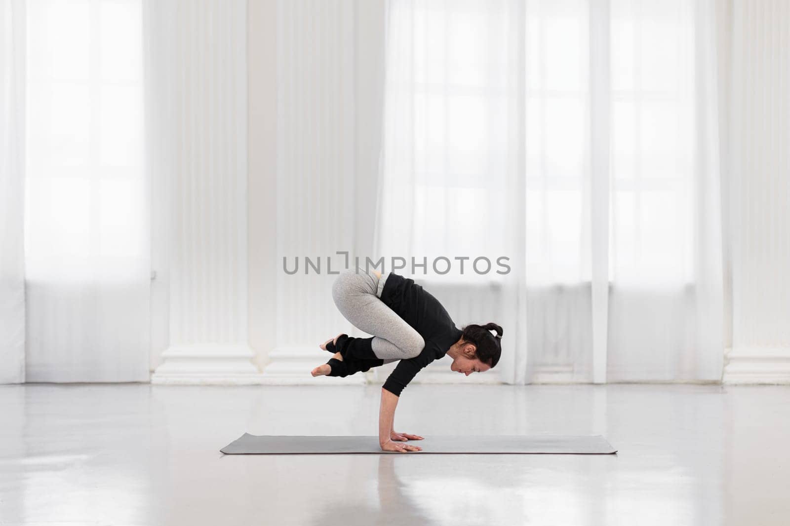Side view of charming woman doing bakasana during yoga meditation in a bright gym. The concept of arm strength and endurance, flexibility and balance.
