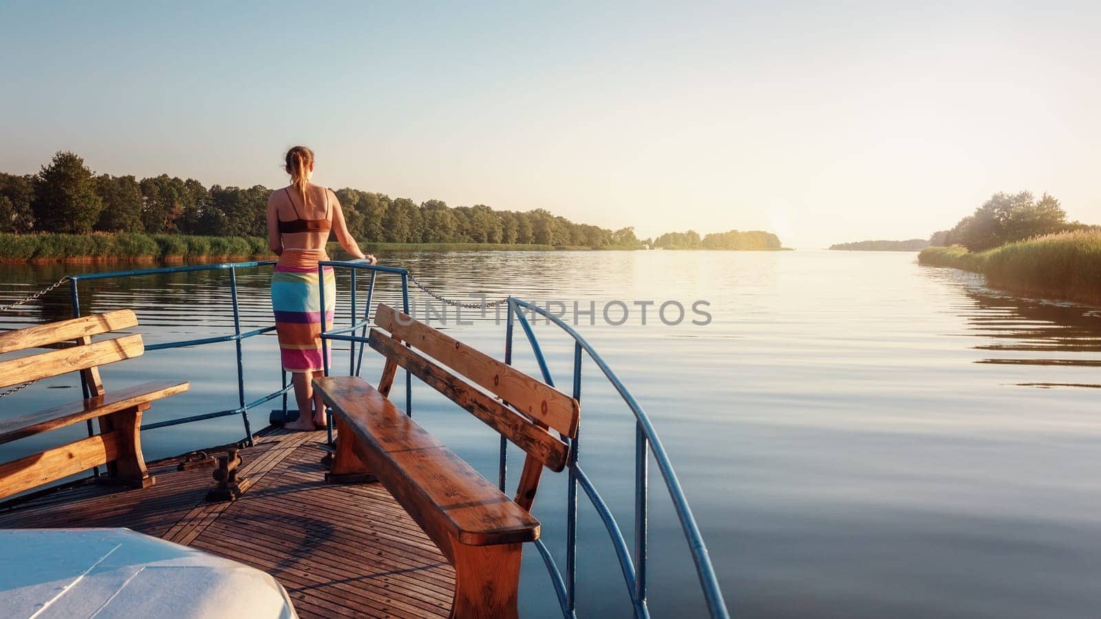 A beautiful young girl stands at the front of the ship and watches the quiet evening sunset