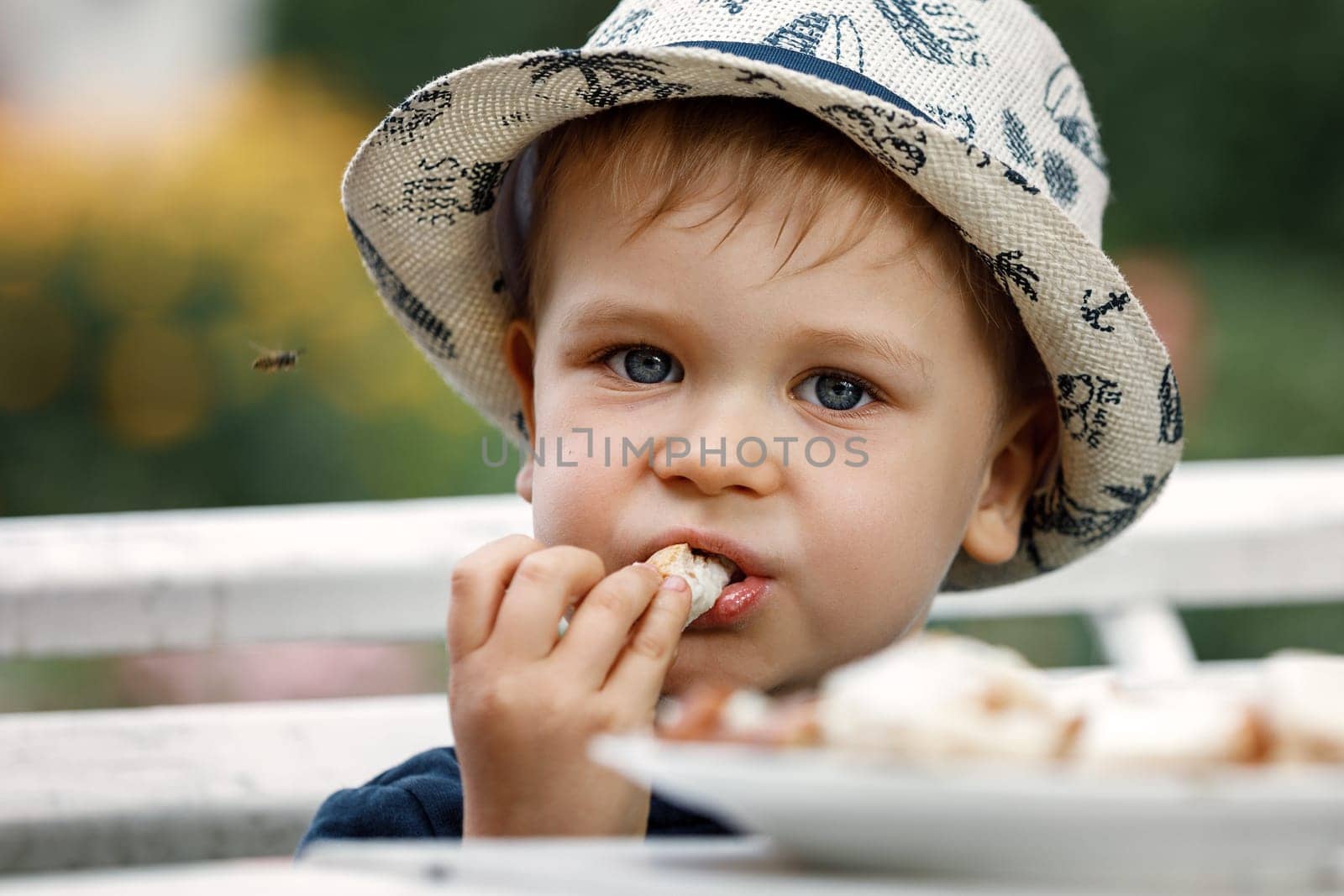 A child eats bread with melted cheese in garden on a summer day by Lincikas