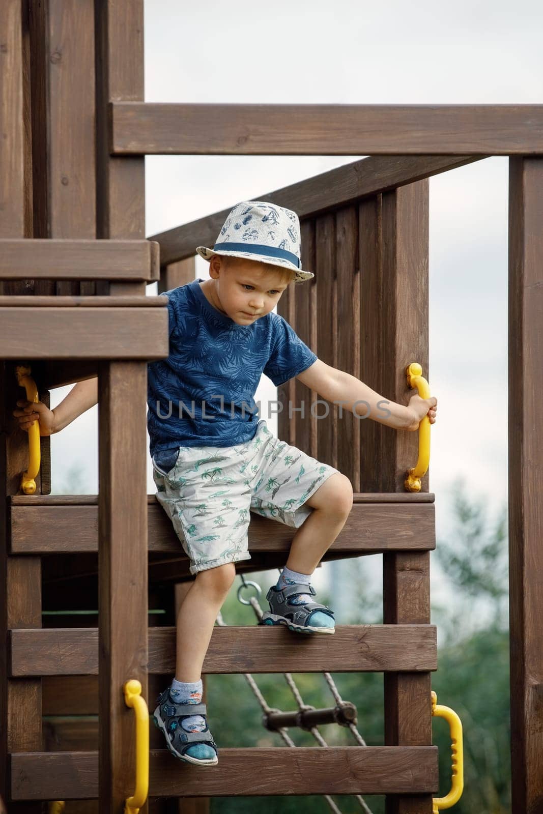 The boy is playing on an outdoor playground, he climbs a wooden ladder dangerously. An active child needs parental care for safety.