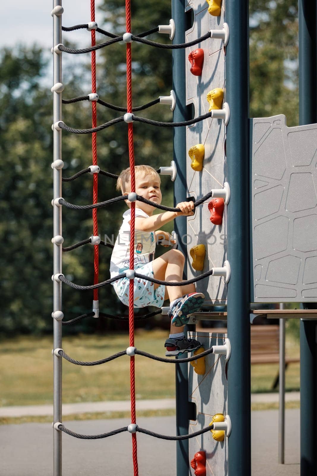 A little boy climbs up a climbing wall on an outdoor playground.