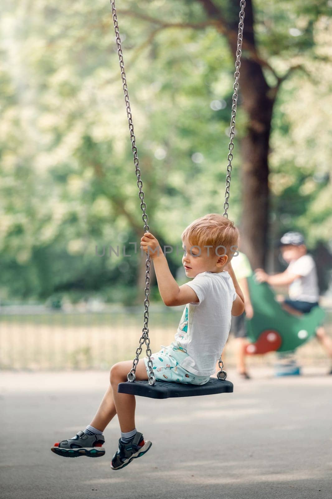 Happy little boy swinging on chain swing at playground.