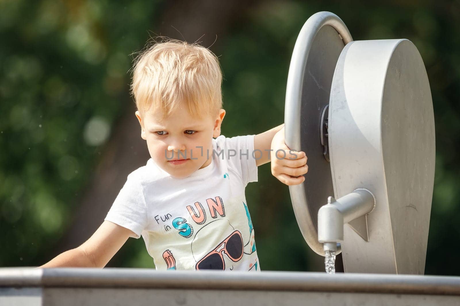 Outdoor portrait of happy little boy playing inside of city fountain on a hot summer day