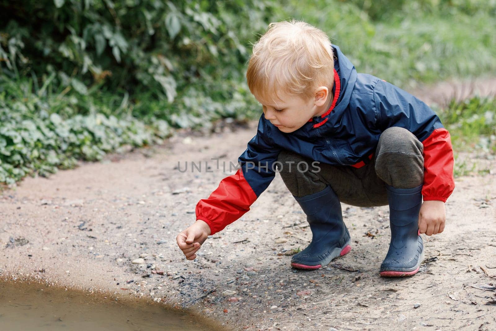 A child squat in a nature explores a dirty swamp, the little one smears his hands and face.