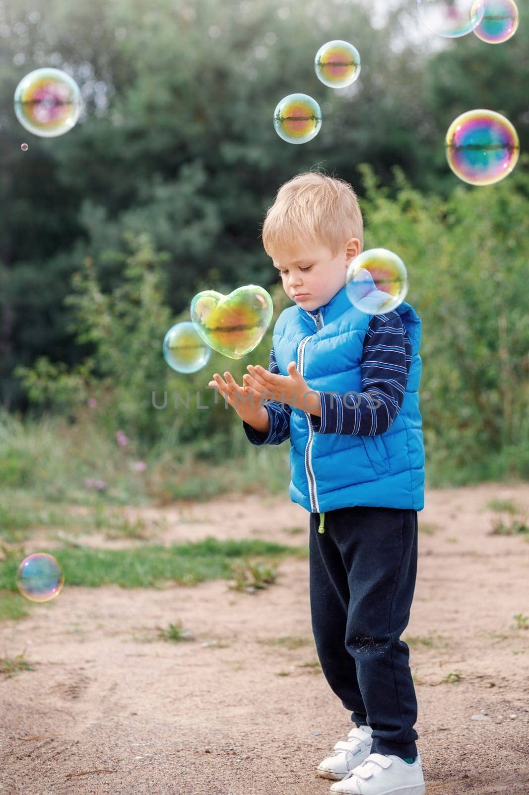 A happy boy catches a heart-shaped soap bubble, a child plays in the park, light balloons float in the air by Lincikas