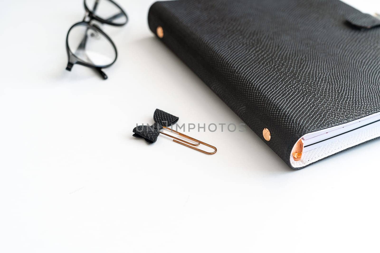 Close up picture of black notepad on white table with glasses aside. Mockup blank space copy space black notebook planner journal.