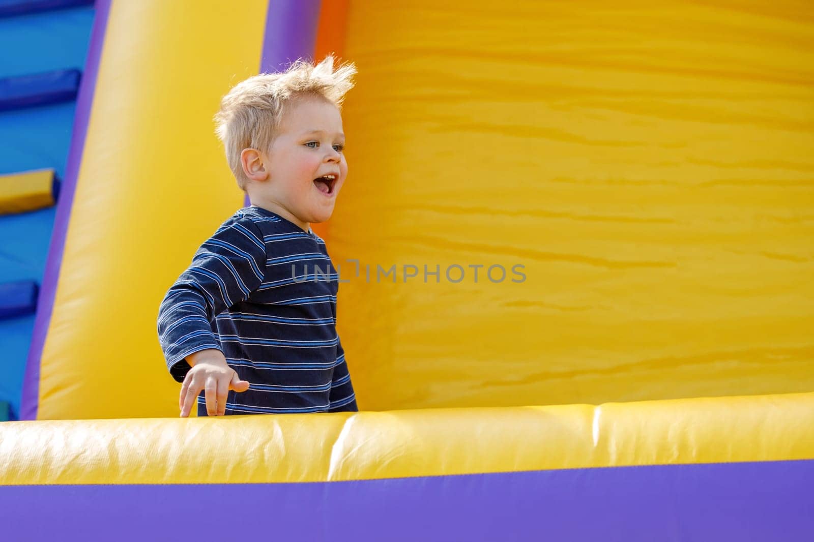 Little cool boy have fun and raging on an yellow inflatable trampoline. There is free space for text in the image by Lincikas