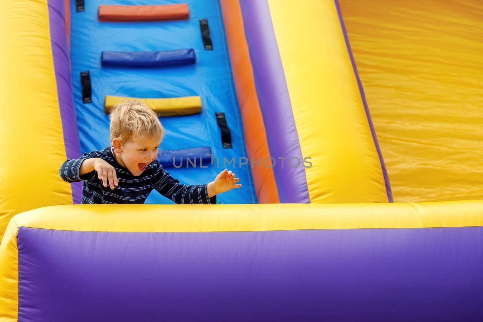 Little boy having fun on inflatable obstacle course. Joyful child naughty, intense raging on colorful inflatable trampoline with ladder. Children's leisure.