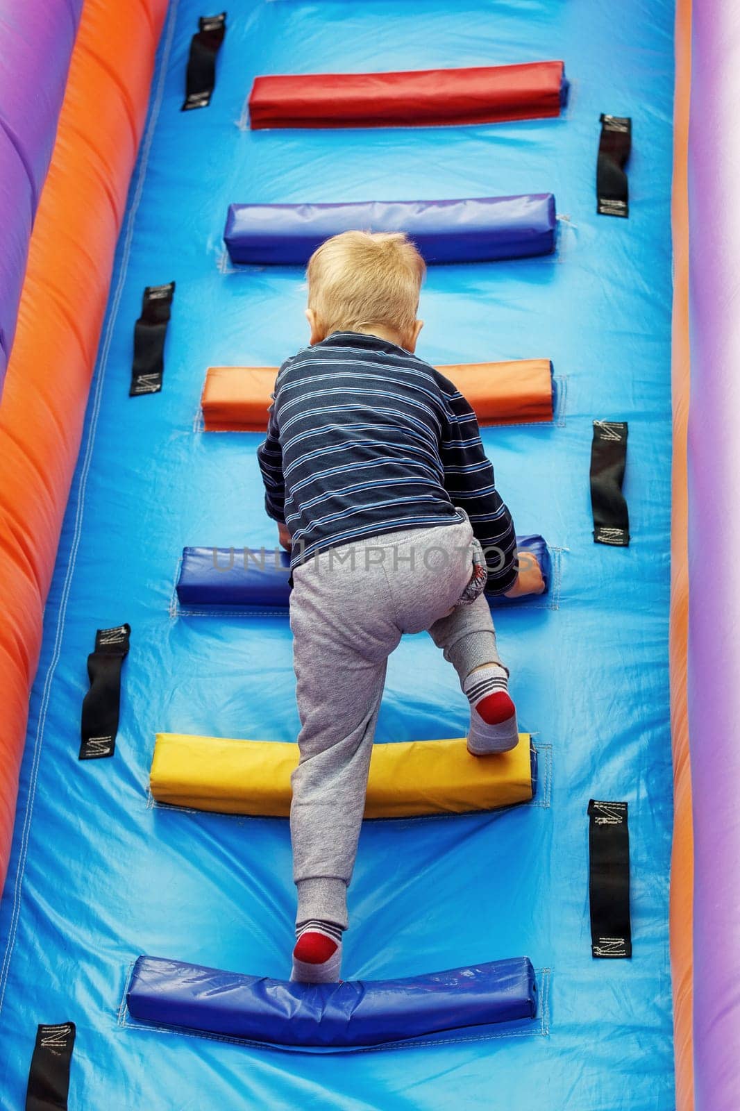 Brave little boy child climbs the stairs of a multi-colored slide in the attraction park by Lincikas