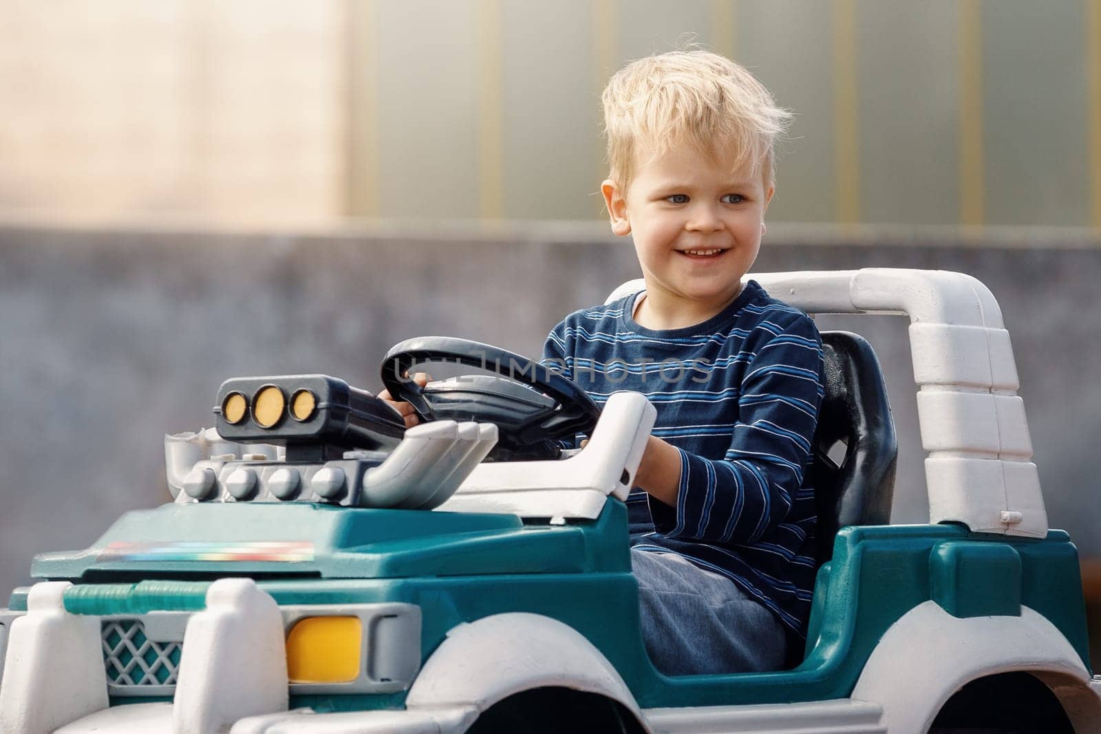 Smiling little boy driving big toy car. Child enjoying warm summer day. Copy space.