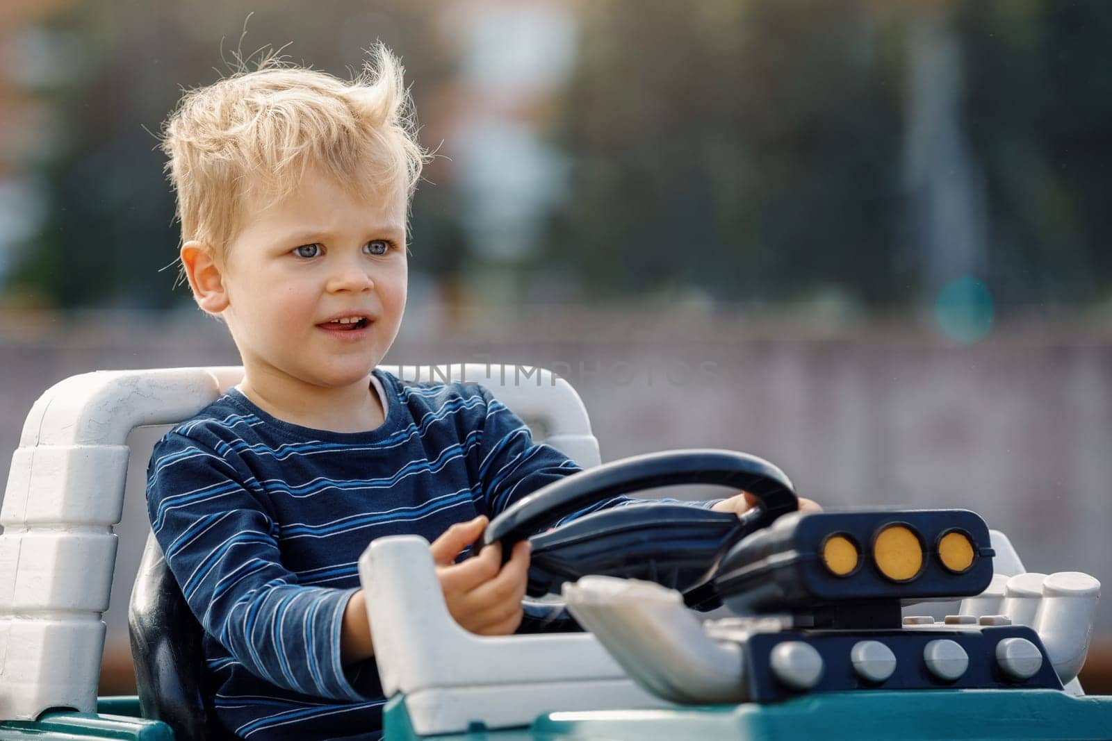 Little boy driving big toy car with steering wheel and having fun outdoors. Young kid portrait with toy car.
