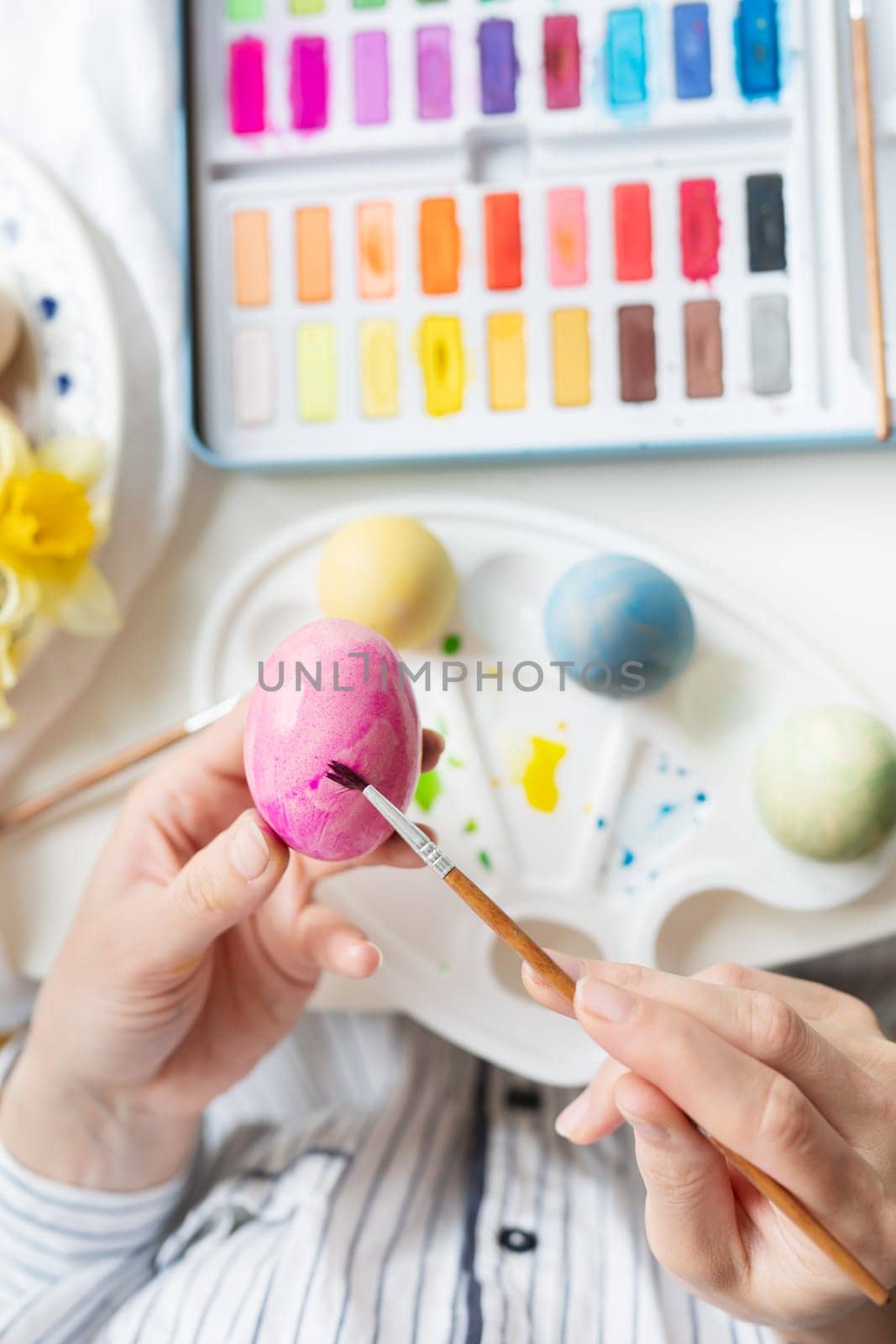 A brush in the process of painting Easter eggs with watercolors. Top view, vertical photo. by sfinks