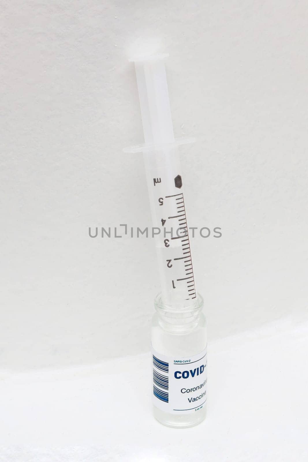 Vertical photo of Covid-19 vaccine bottle and syringe against white wall. Pharmoceutical concept.
