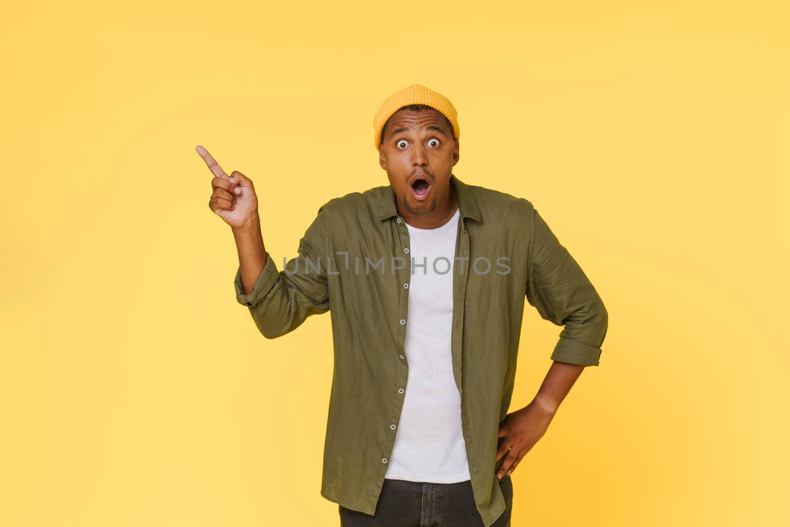 Amazed African man points to the side to copy space on yellow background. Advertising concept. by LipikStockMedia