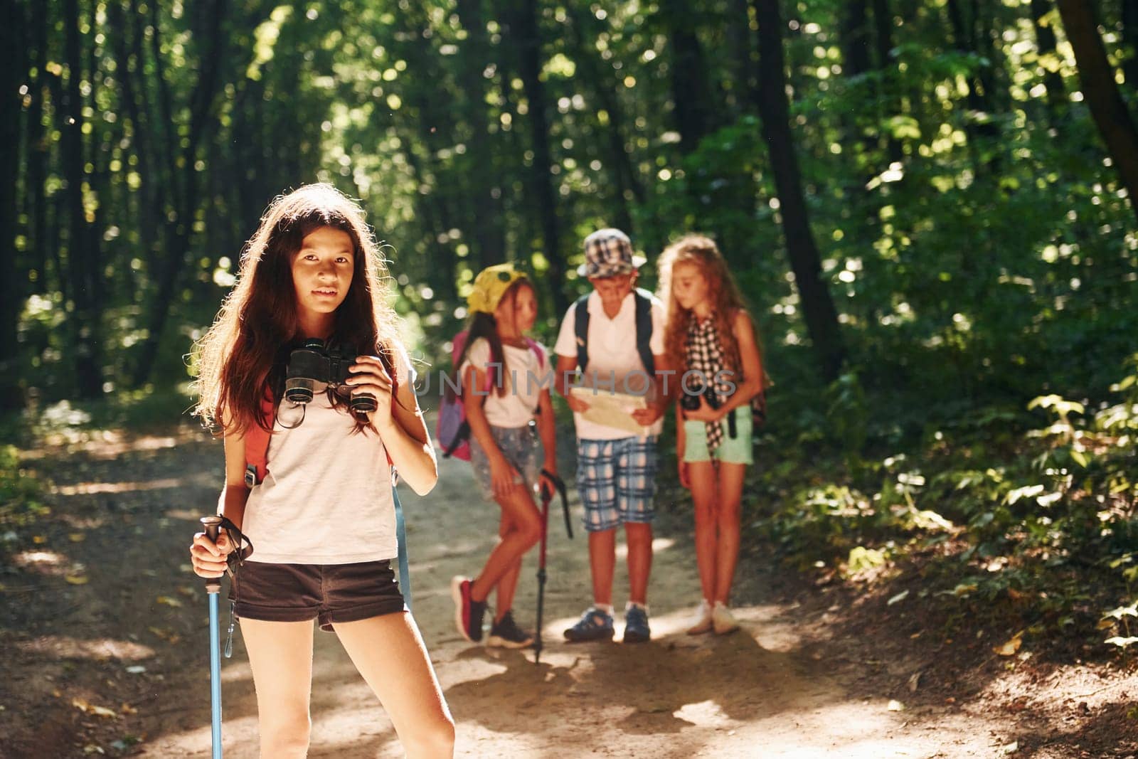 Girl standing in front of her friends. Kids strolling in the forest with travel equipment by Standret