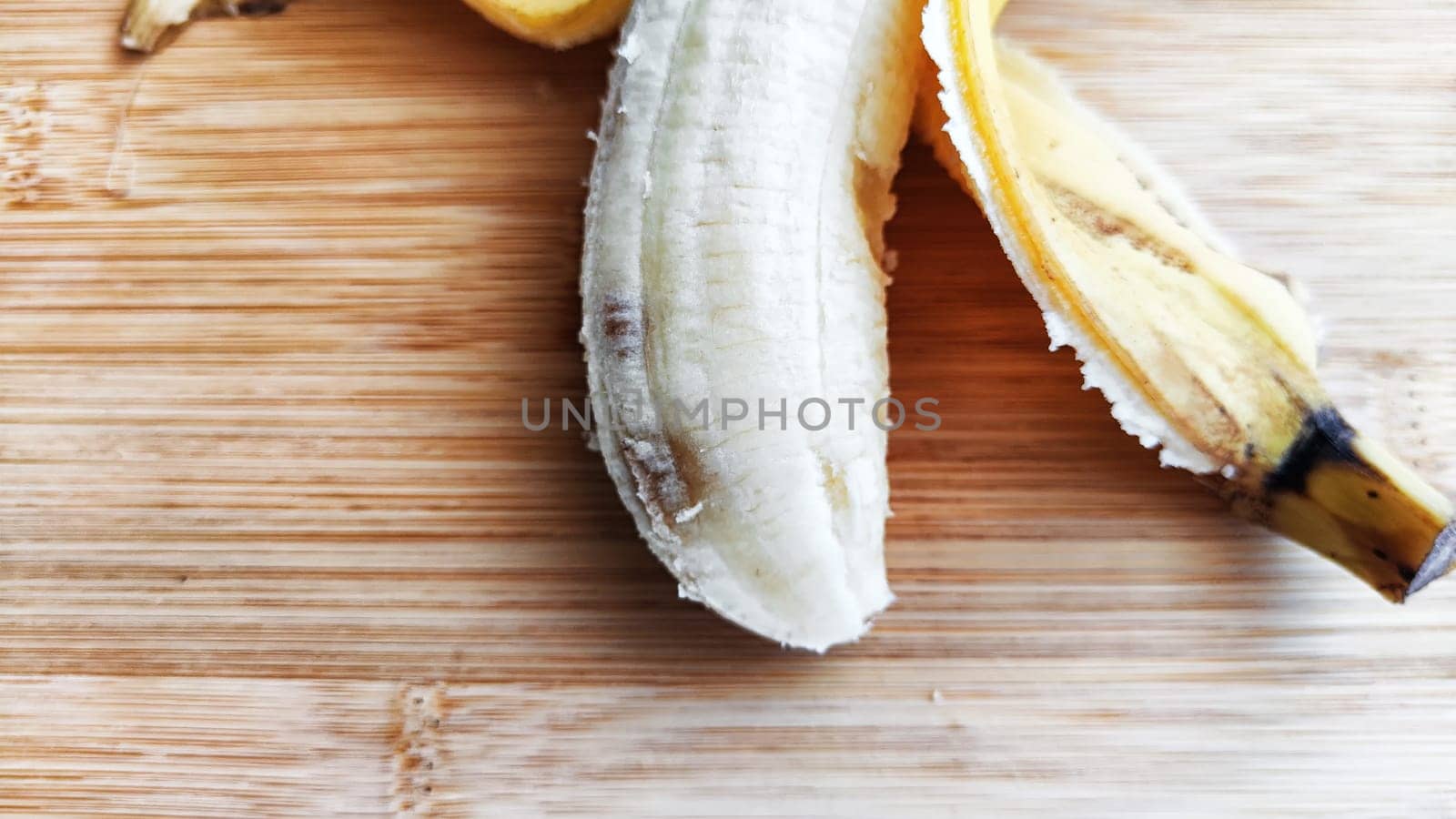 Banana with open peel on wooden board and white background. Ripe banana with peel, Close up. Delicious sweet fruit dessert