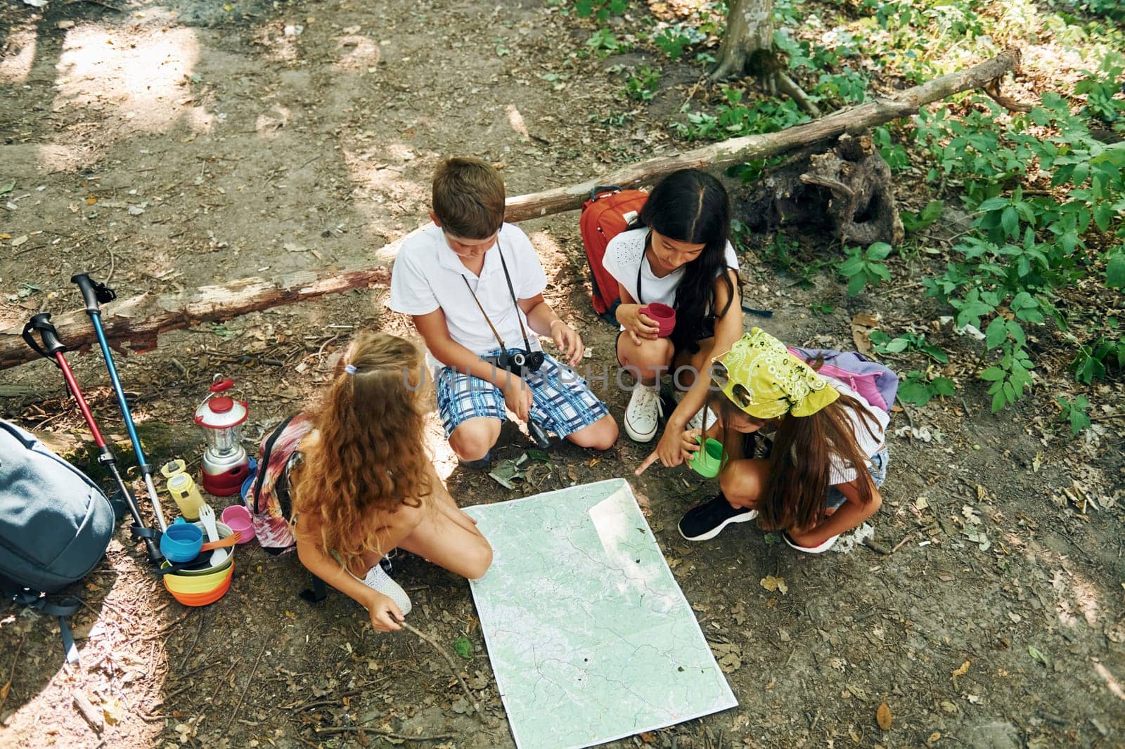 Sitting on the ground. Kids strolling in the forest with travel equipment by Standret