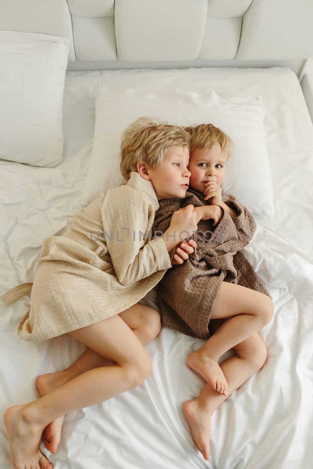 Boys, brothers lie on the bed in dressing gowns after a shower.
