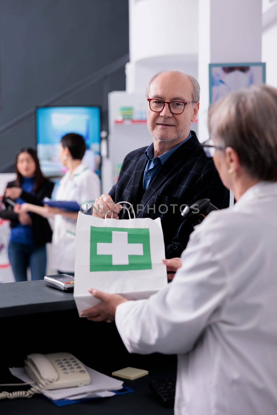 Chemist giving old man drugstore online order at checkout, holding paper bag with customer purchase. Elderly buyer in glasses visiting apothecary and taking medications package at paydesk