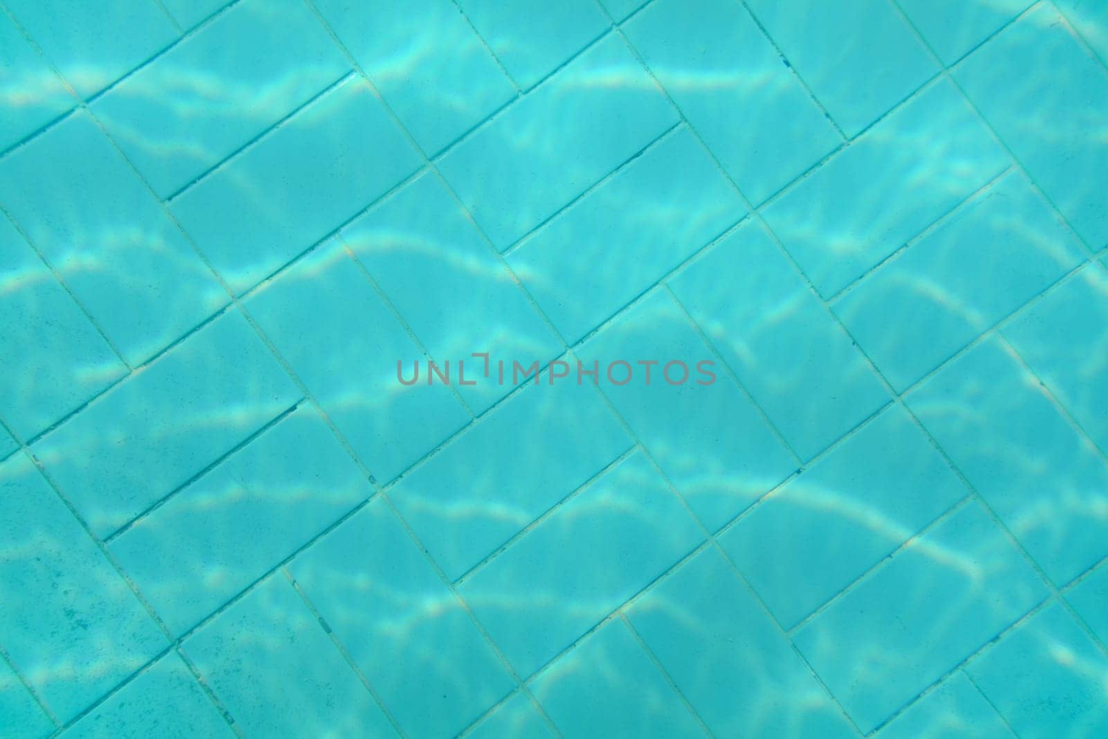 Underwater photo - old swimming pool bottom. Blue tiles pattern visible on floor. Abstract water background.