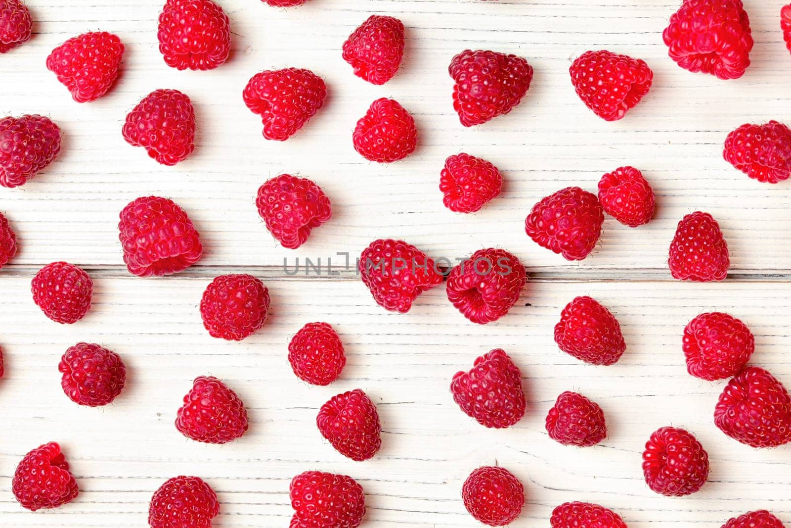 Tabletop view, raspberries spilled on white boards desk.