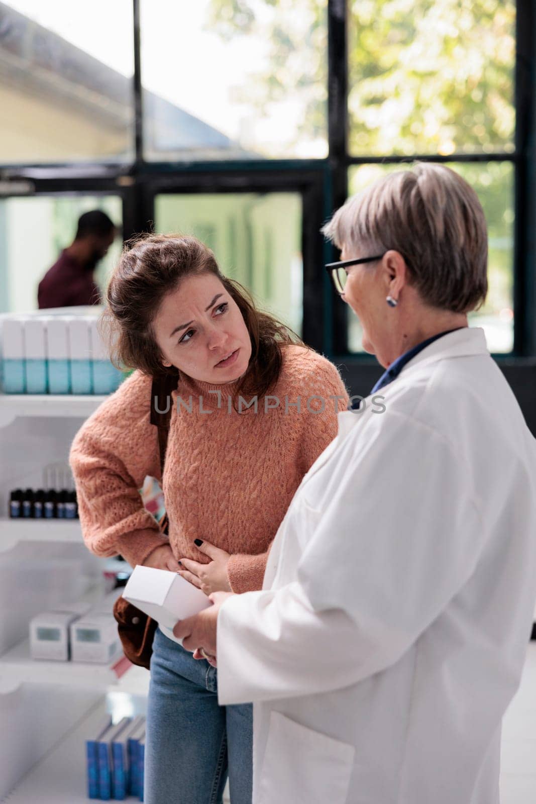Drugstore worker helping sick adult client with abdominal cramps offering stomachache medication by DCStudio