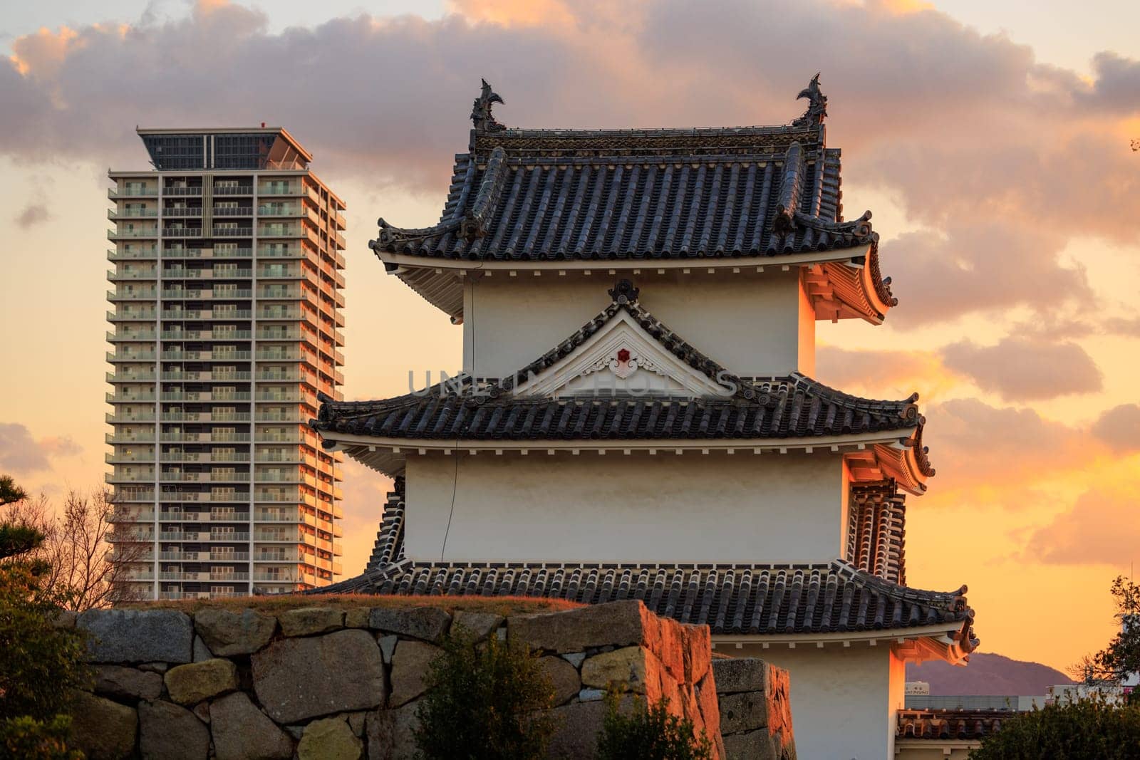 Sunset over watchtower in Japanese castle and modern high rise apartment building by Osaze