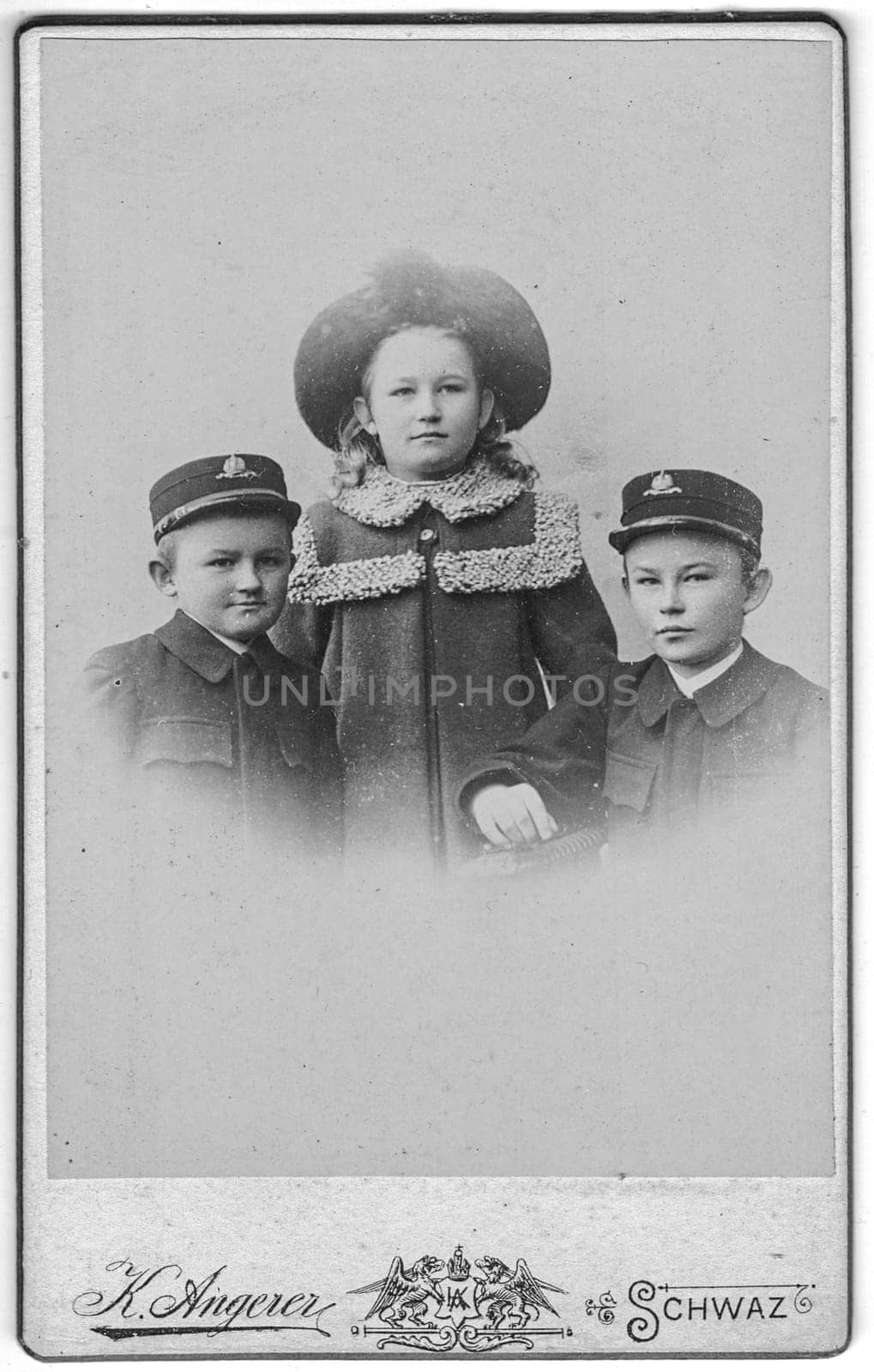 SCHWAZ - TIROL, AUSTRIA-HUNGARY - CIRCA 1900: Vintage cabinet card shows portrait of cute siblings two brothers and hers sister. Edwardian fashion. Photo was taken in a photo studio. Photo was taken in Austro-Hungarian Empire or also Austro-Hungarian Monarchy