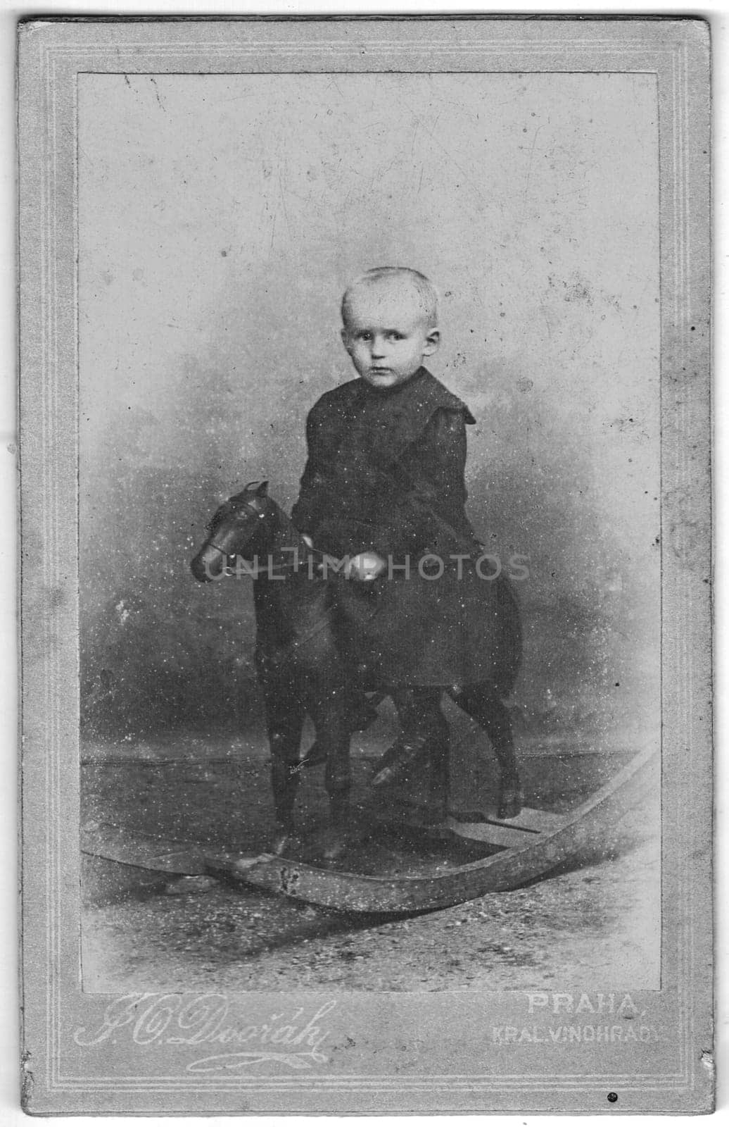 Vintage cabinet card shows portrait of the small child. Little boy sitting on rocking horse. Edwardian fashion. Photo was taken in a photo studio. Photo was taken in Austro-Hungarian Empire or also Austro-Hungarian Monarchy by roman_nerud