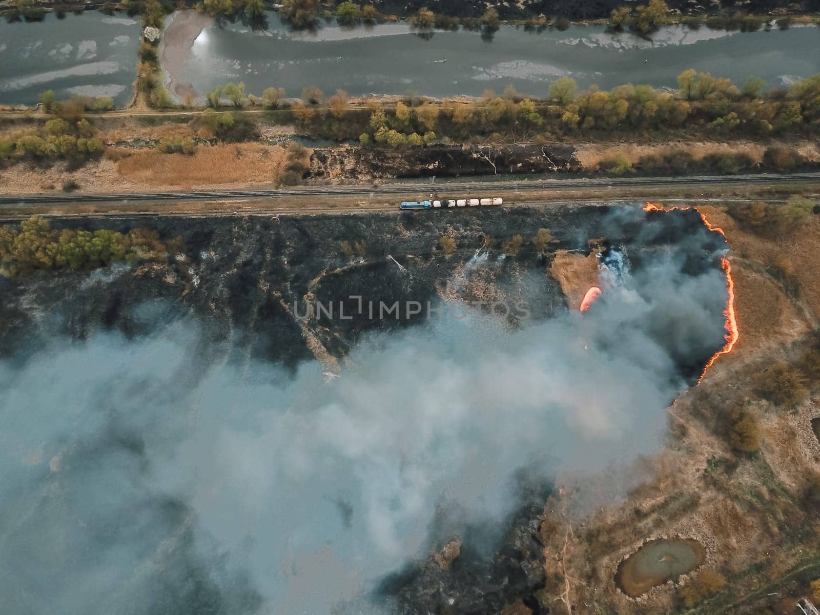 Aerial drone flight over burning hill side with thick white smoke blown off frame . Natural disaster due to extreme heat and climate change