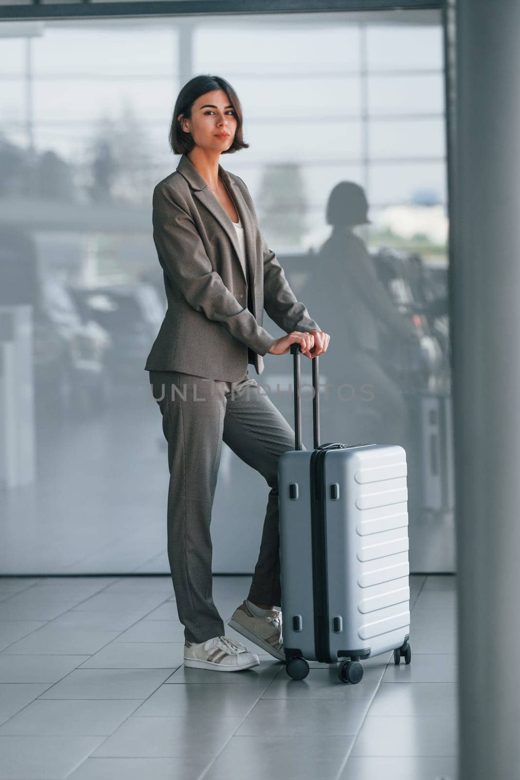 In formal clothes. Woman with luggage is standing indoors. Conception of tourism.