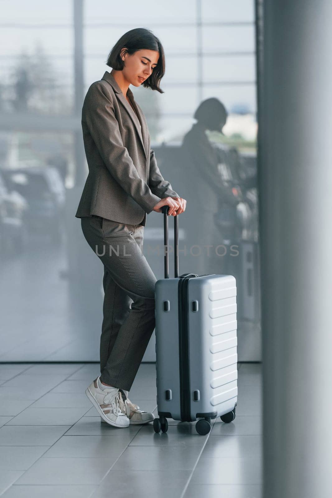 Against wall with reflection. Woman with luggage is standing indoors. Conception of tourism.