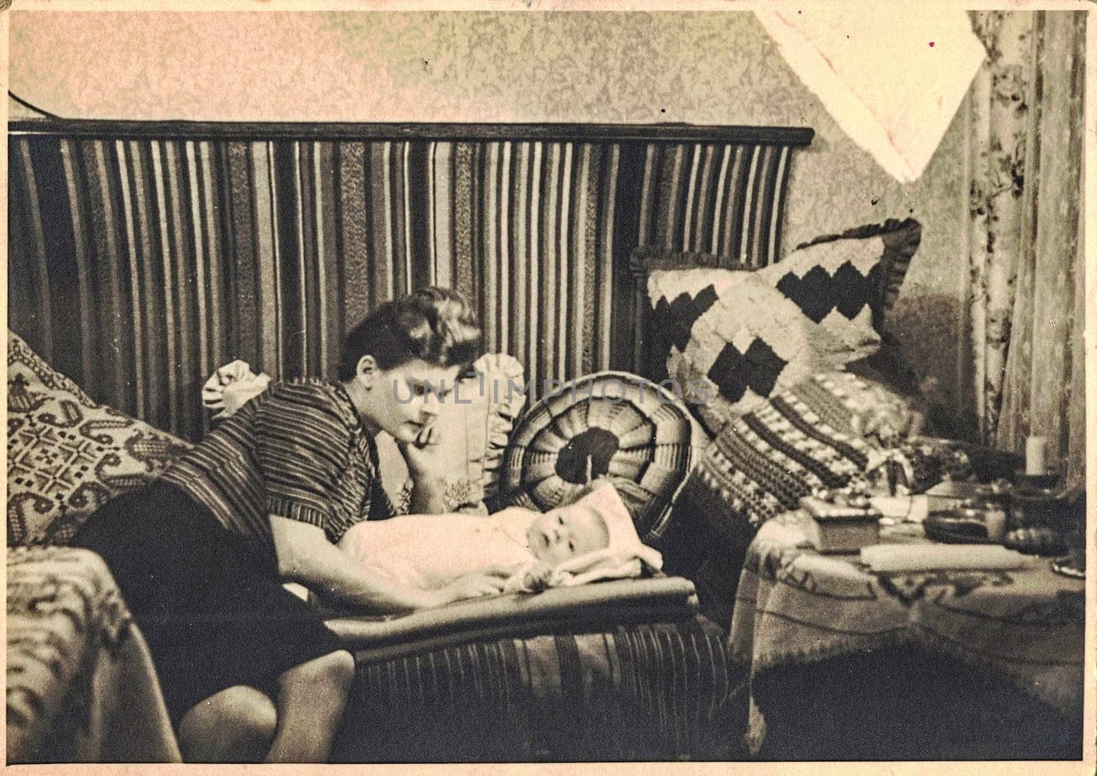 NEURUPPIN, EASTERN GERMANY - CIRCA 1960s: Retro photo shows happy mum with baby child. The sixties and knitted pillow in Socialist bloc.