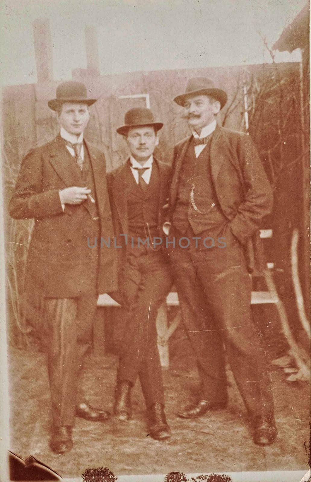 Vintage cabinet card shows dandy men wear bowler hats, luxury garment and one holds cigar. Antique black and white photo. Original photo with imperfection. by roman_nerud