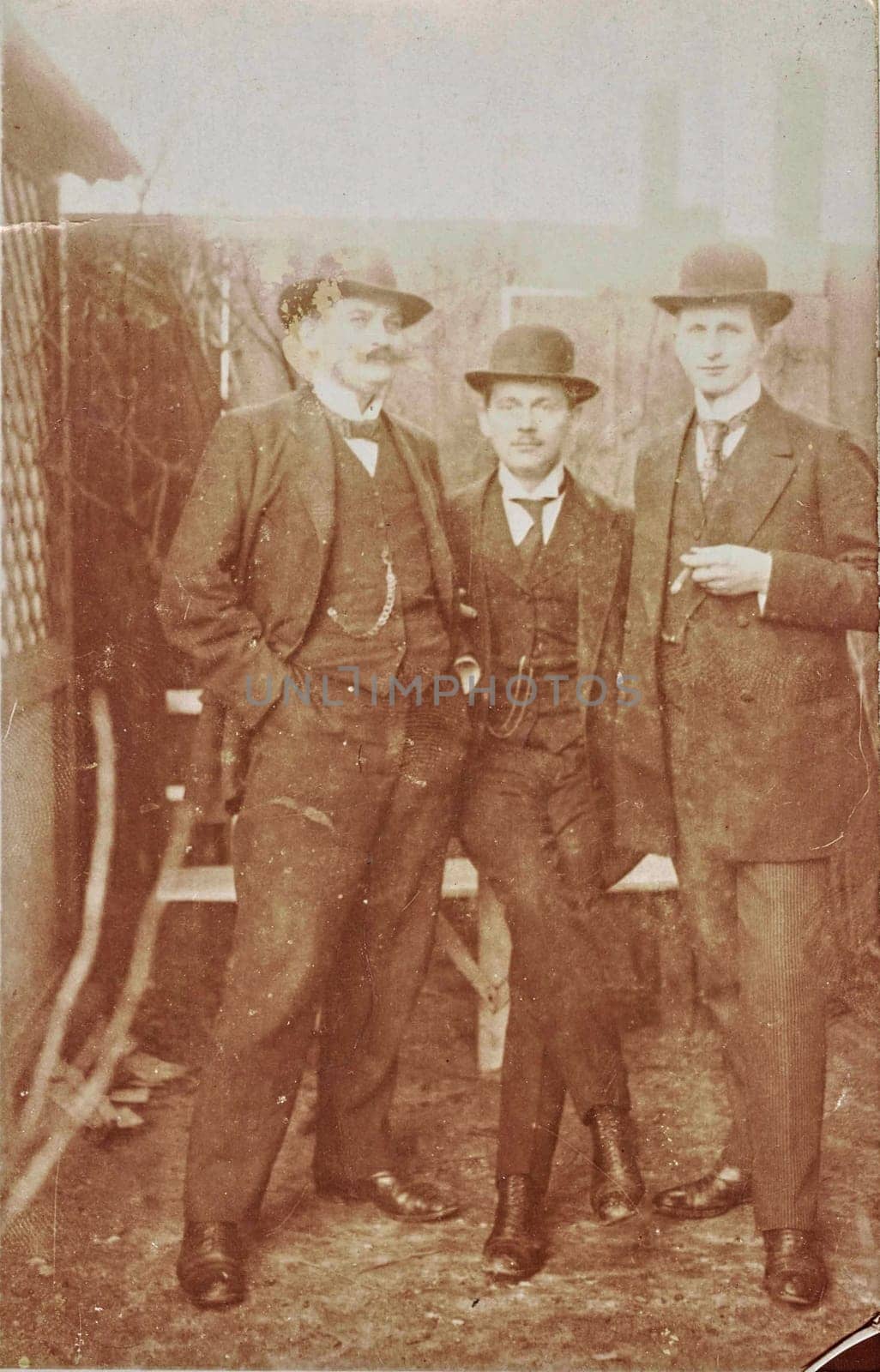 GERMANY - CIRCA 1905: Vintage cabinet card shows dandy men wear bowler hats, luxury garment and one holds cigar. Antique black and white photo. Original photo with imperfection.