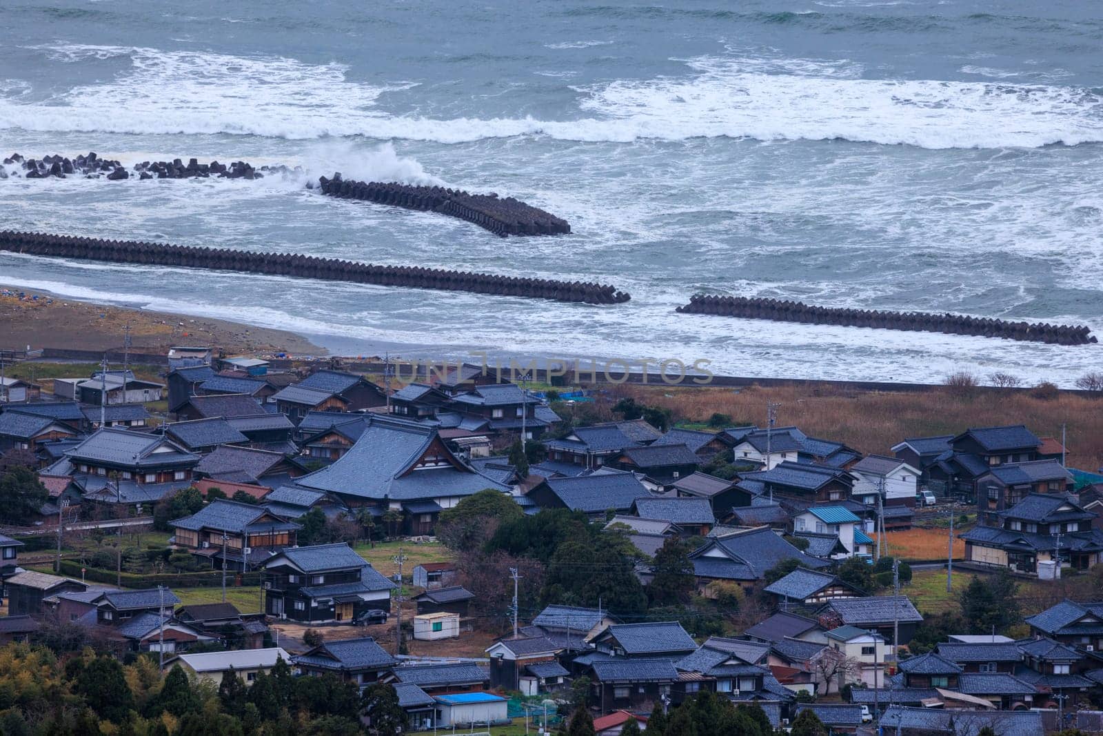 Waves hit concrete breakwater protecting small coastal village by Osaze