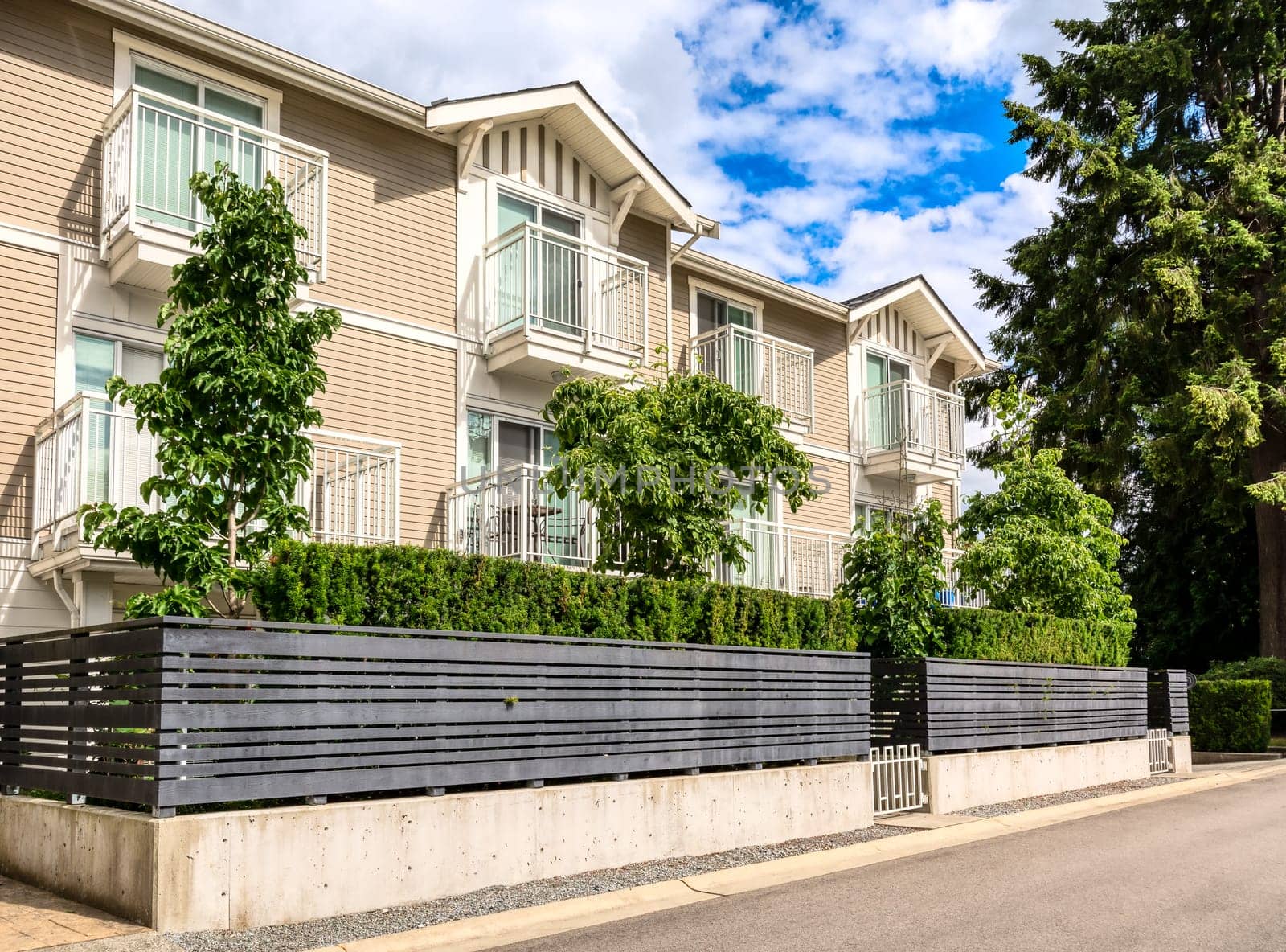 Residential condo building with fenced front yard on bright sunny day in British Columbia