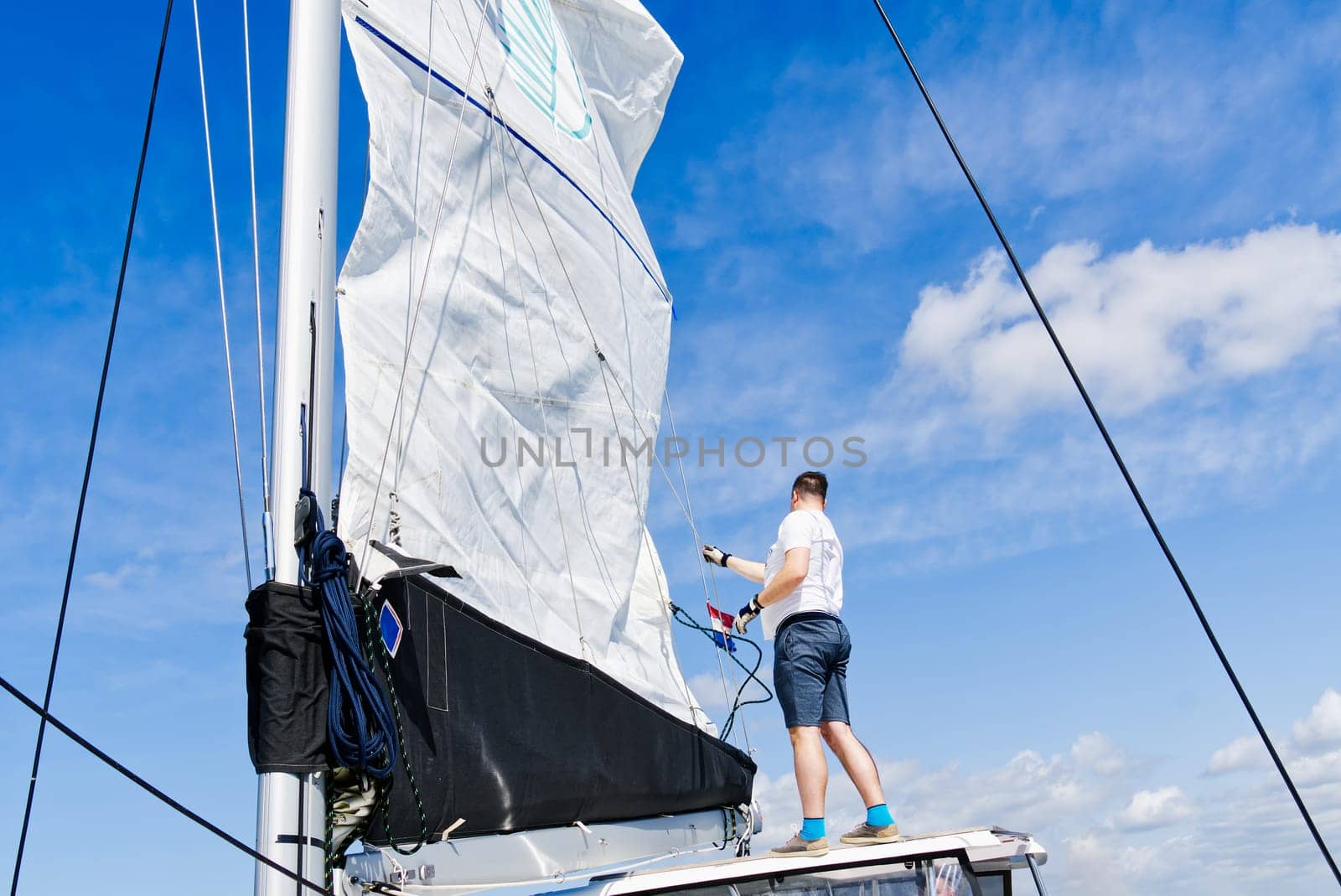 Raising the sail on a yacht. Young man captan lifting the sail of catamaran yacht during cruising. luxury sailing yacht, with sails being raised by rigging