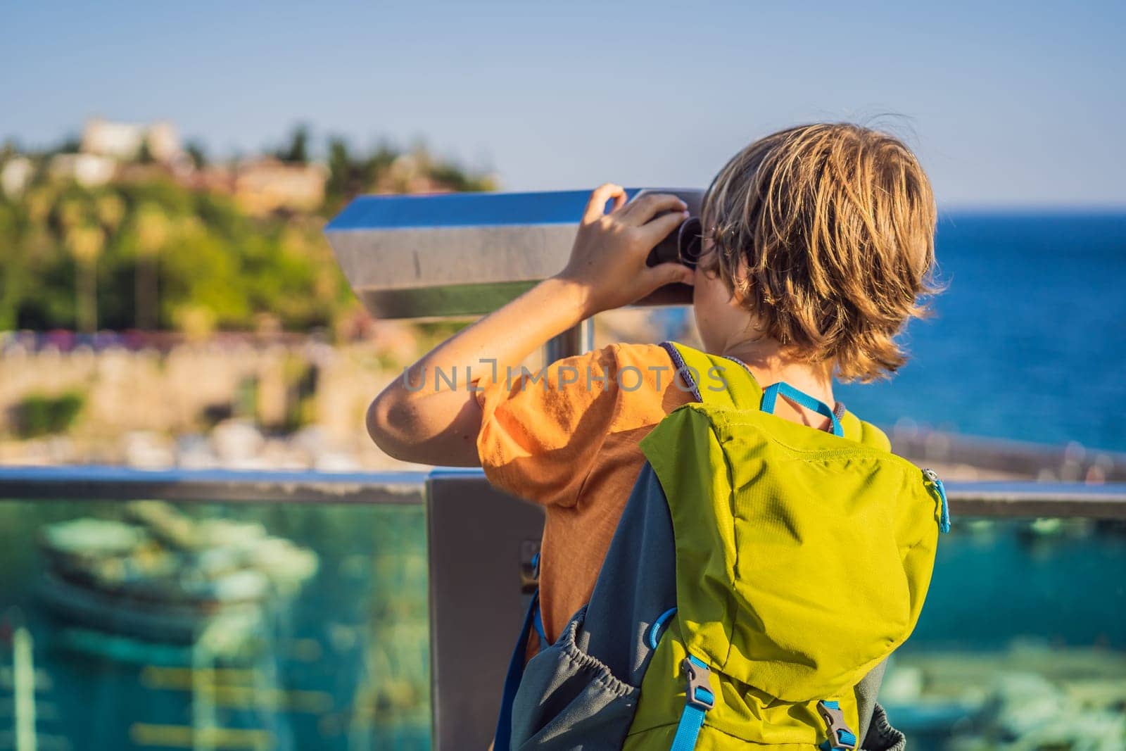 Boy tourist looks through binoculars in Old town Kaleici in Antalya. Turkiye. Panoramic view of Antalya Old Town port, Taurus mountains and Mediterrranean Sea, Turkey. Traveling with kids concept.