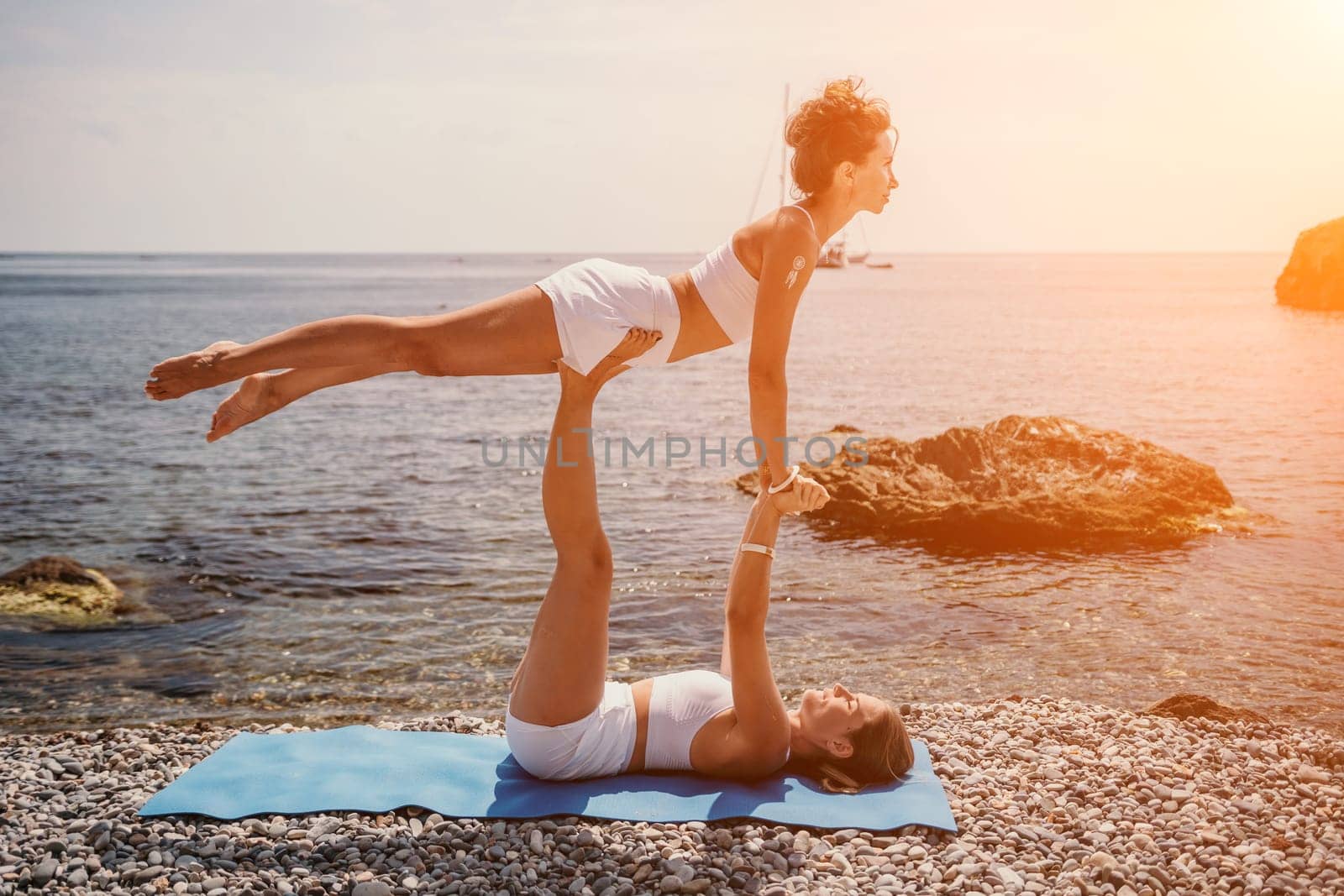 Woman sea yoga. Two Happy women meditating in yoga pose on the beach, ocean and rock mountains. Motivation and inspirational fit and exercising. Healthy lifestyle outdoors in nature, fitness concept. by panophotograph