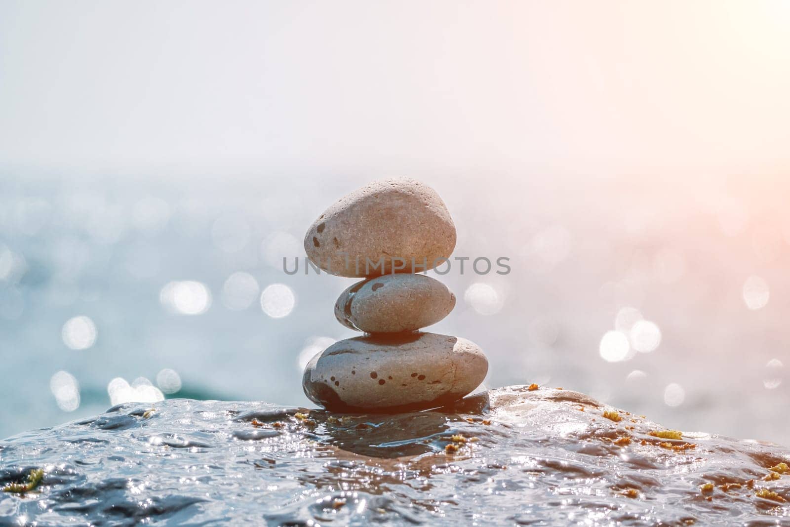 Balanced rock pyramid on sea pebbles beach, sunny day and clear sky at sunset. Golden sea bokeh on background. Selective focus, zen stones on sea beach, meditation, spa, harmony, calm, balance concept by panophotograph