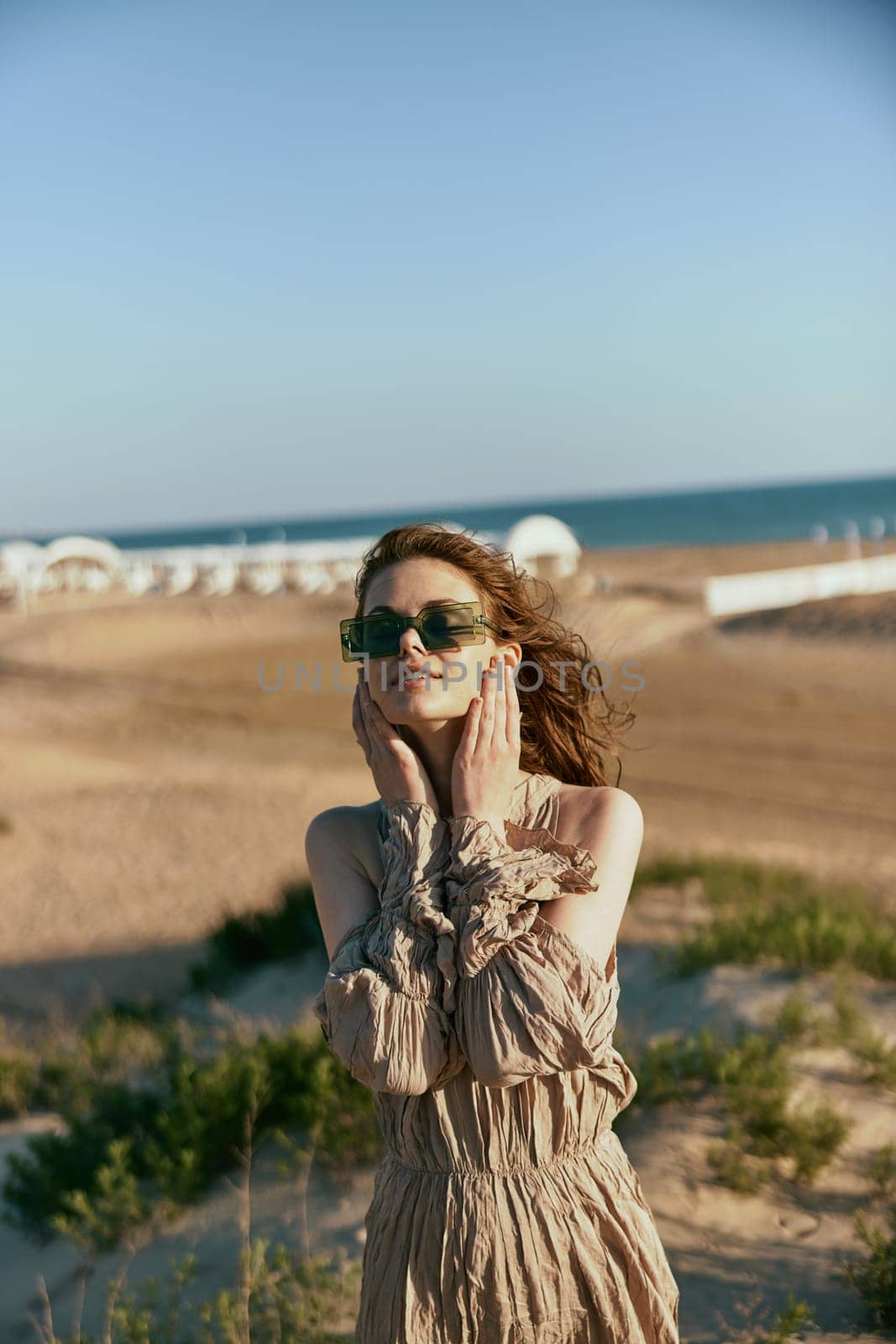 portrait of a smiling woman in a light dress and sunglasses holding her hands near her face by Vichizh