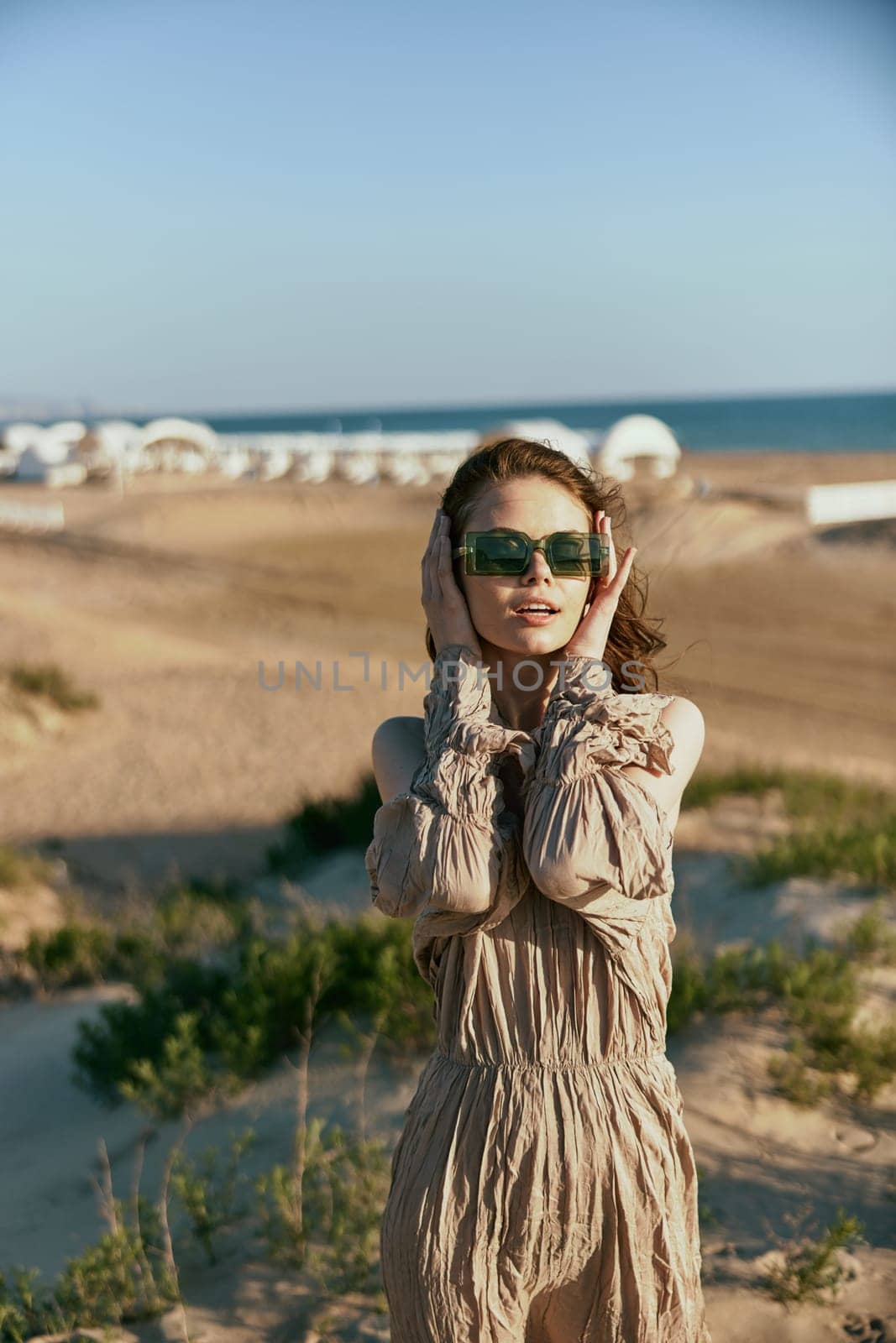 portrait of a smiling woman in a light dress and sunglasses holding her hands near her face. High quality photo