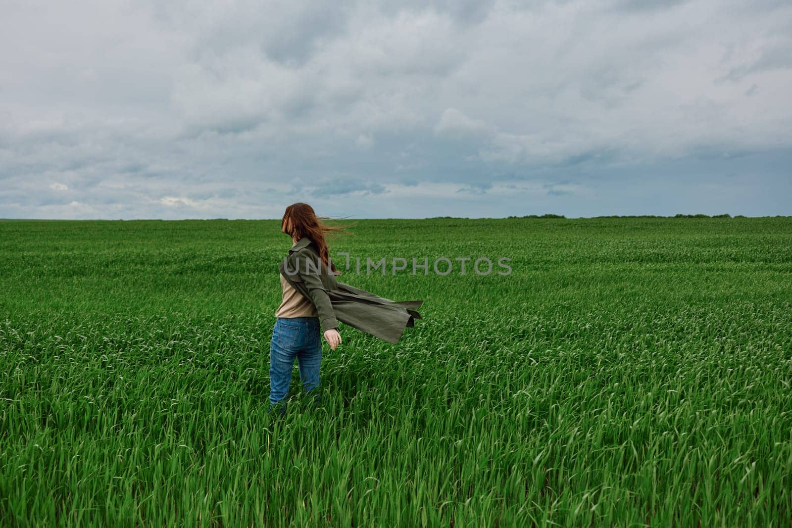 a woman in a dark coat walks through a field with tall grass in windy, rainy weather. High quality photo